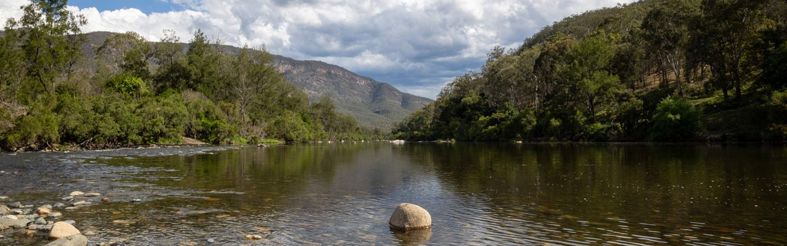 An image of the Macleay River with green hills and a cloudy sky in the distance.