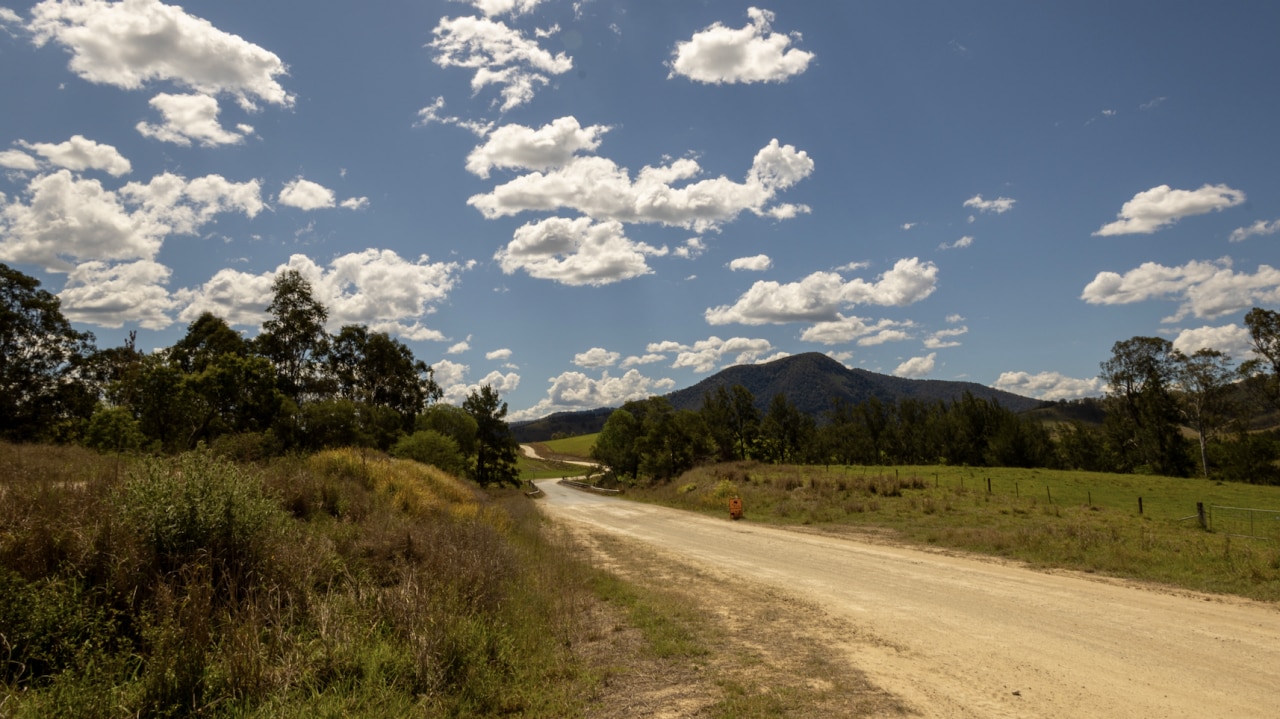A single track road against green hills and a blue sky with wispy clouds.